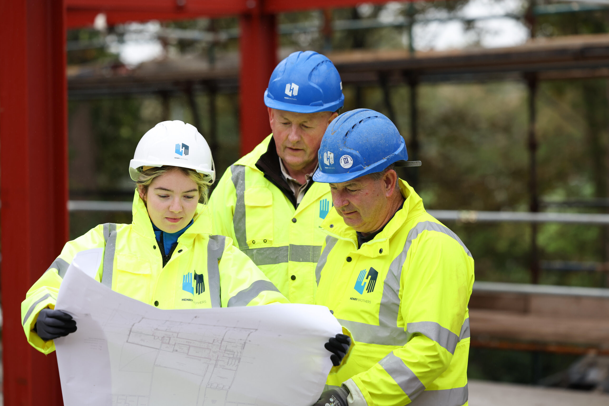 Young girl and 2 men wearing hard hats and Hi-vis on construction site